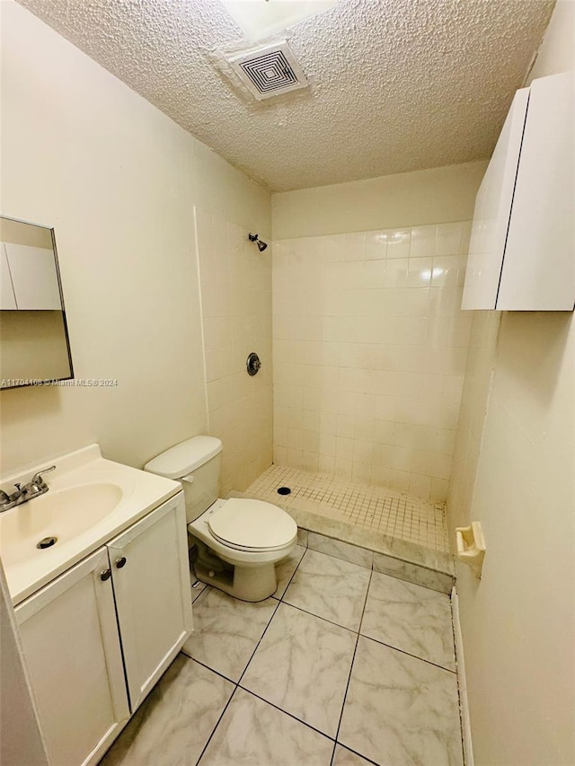 bathroom with vanity, a tile shower, a textured ceiling, and toilet