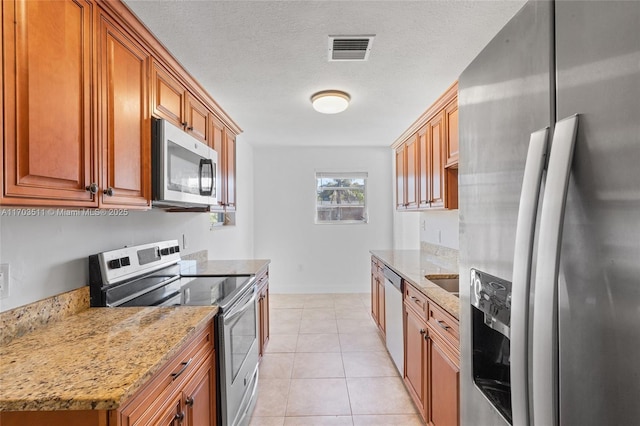 kitchen with light stone counters, light tile patterned floors, stainless steel appliances, and a textured ceiling