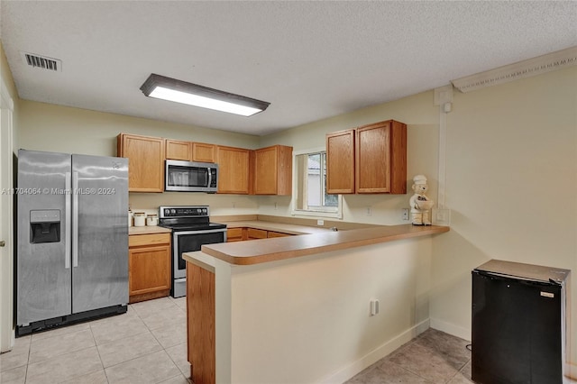 kitchen featuring kitchen peninsula, light tile patterned floors, stainless steel appliances, and a textured ceiling