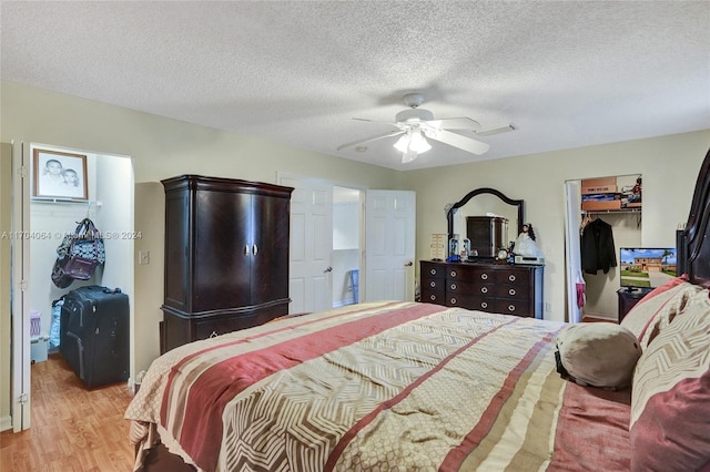 bedroom with ceiling fan, a textured ceiling, a walk in closet, a closet, and light wood-type flooring