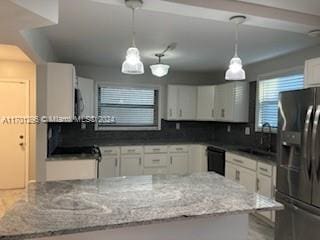 kitchen featuring dark stone counters, fridge with ice dispenser, black dishwasher, white cabinetry, and hanging light fixtures