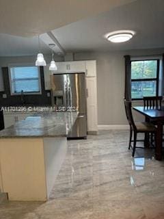 kitchen featuring decorative light fixtures, stainless steel fridge, light stone counters, and white cabinetry