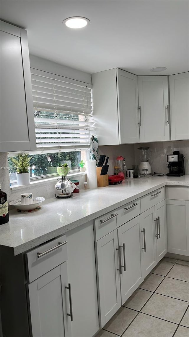 kitchen with backsplash, light stone counters, a wealth of natural light, light tile patterned floors, and white cabinetry