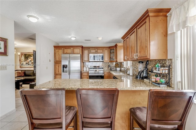 kitchen featuring sink, stainless steel appliances, kitchen peninsula, a textured ceiling, and a kitchen bar