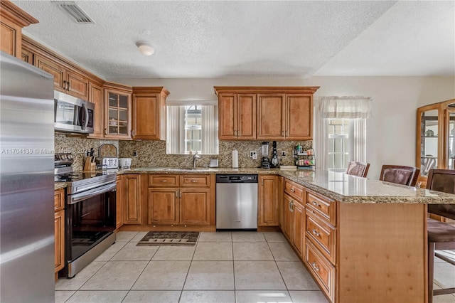 kitchen featuring kitchen peninsula, a kitchen breakfast bar, appliances with stainless steel finishes, tasteful backsplash, and light tile patterned floors