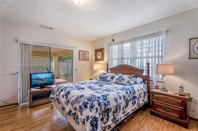 bedroom with access to exterior, a textured ceiling, and light wood-type flooring