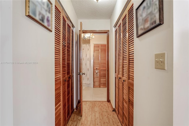 hallway featuring a textured ceiling, light hardwood / wood-style flooring, and a notable chandelier