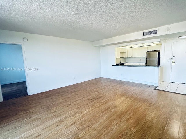 unfurnished living room with a textured ceiling and light wood-type flooring