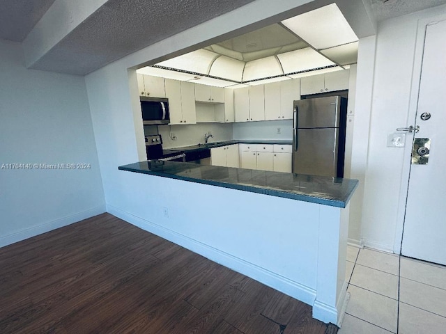 kitchen with kitchen peninsula, a textured ceiling, stainless steel appliances, hardwood / wood-style floors, and white cabinetry