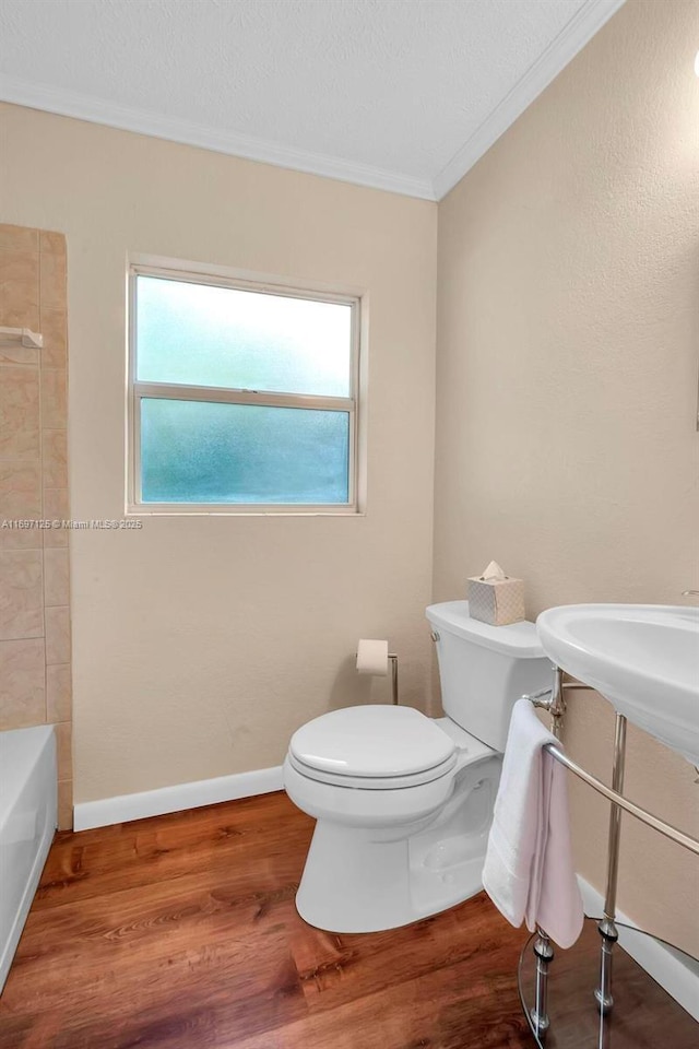 bathroom with wood-type flooring, a bathtub, crown molding, and toilet