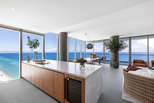 kitchen featuring a water view, a wall of windows, hanging light fixtures, and beverage cooler