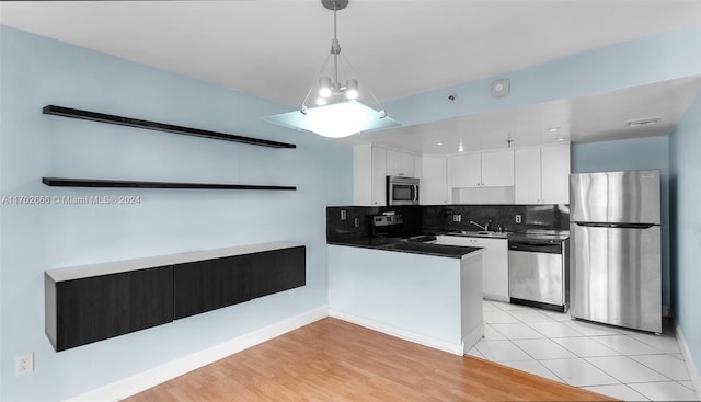 kitchen with light wood-type flooring, appliances with stainless steel finishes, tasteful backsplash, decorative light fixtures, and white cabinetry