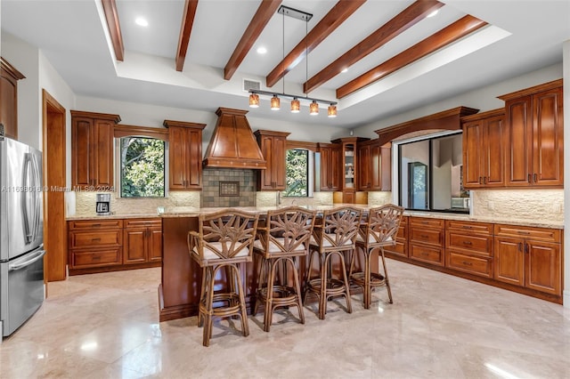 kitchen with stainless steel refrigerator, decorative backsplash, a healthy amount of sunlight, and custom exhaust hood