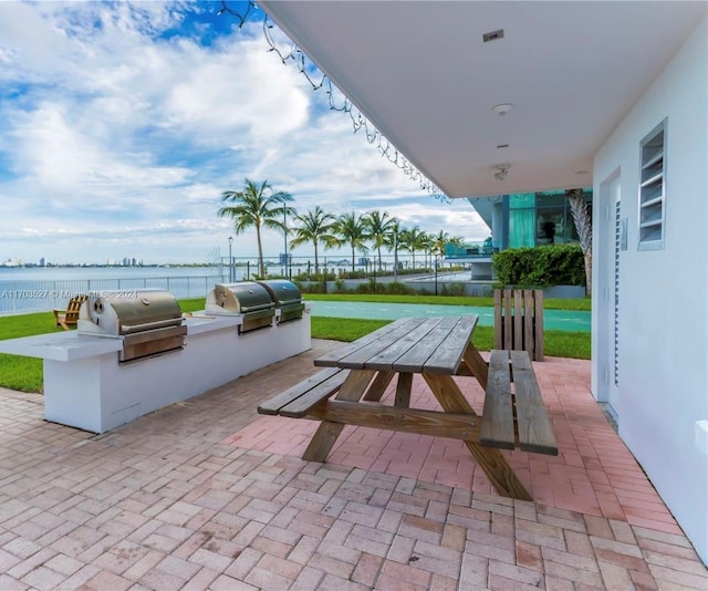 view of patio featuring a grill, a water view, and an outdoor kitchen