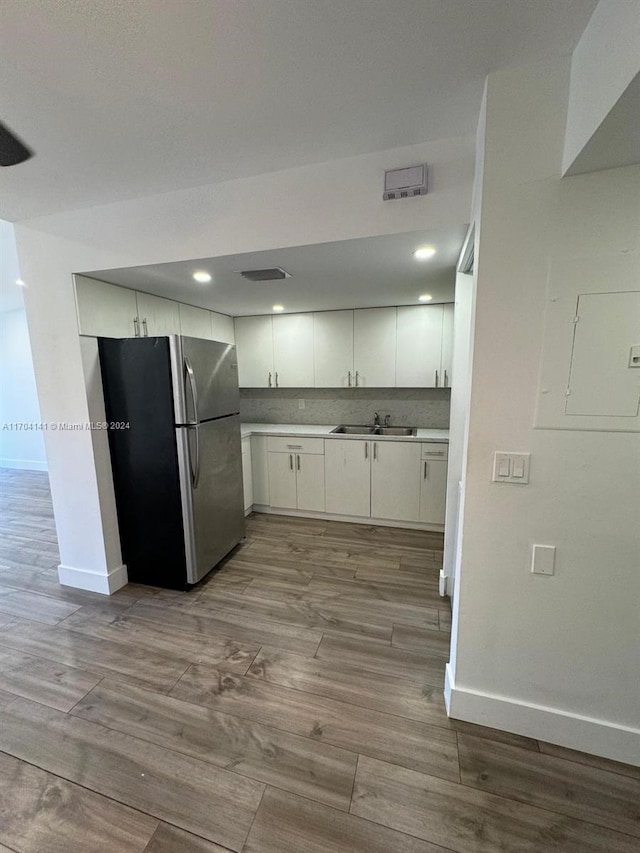 kitchen featuring decorative backsplash, stainless steel fridge, sink, white cabinets, and light hardwood / wood-style floors