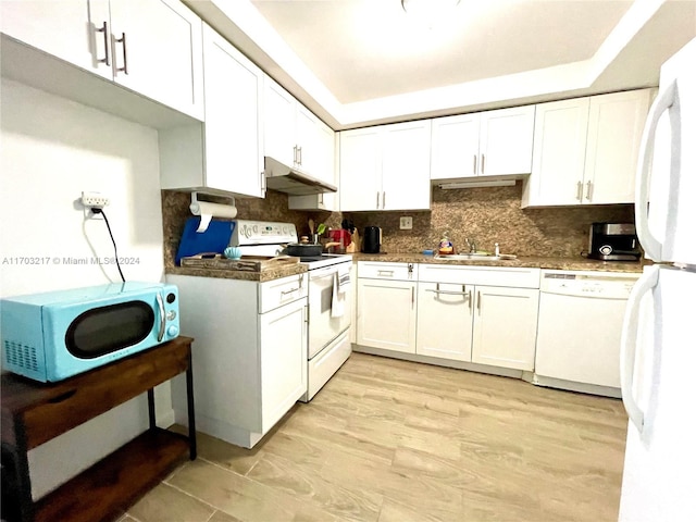 kitchen with tasteful backsplash, white appliances, a tray ceiling, white cabinets, and light wood-type flooring