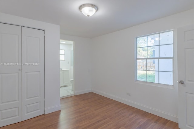 unfurnished bedroom featuring ensuite bathroom, a closet, and wood-type flooring