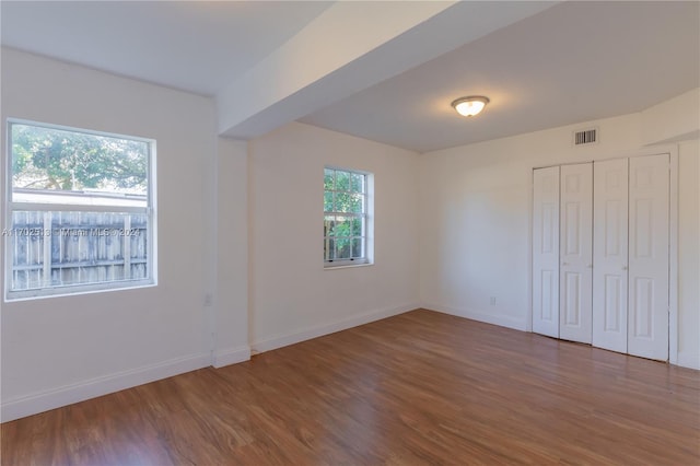 unfurnished bedroom with wood-type flooring, a closet, and multiple windows