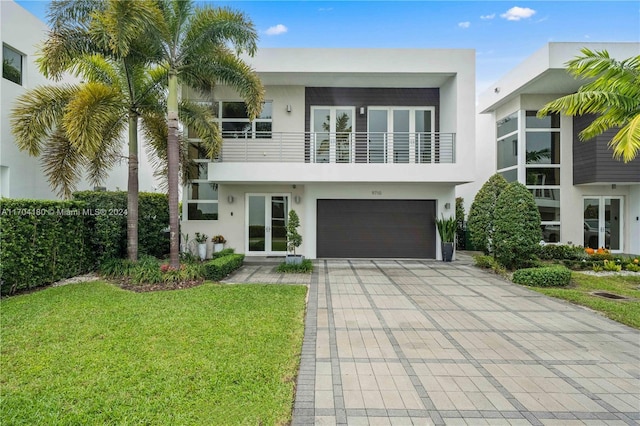 view of front facade with a front yard, french doors, a balcony, and a garage