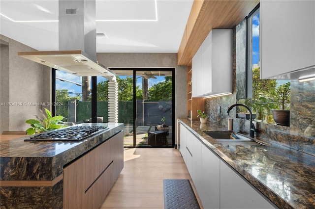 kitchen featuring island exhaust hood, sink, white cabinets, and dark stone countertops