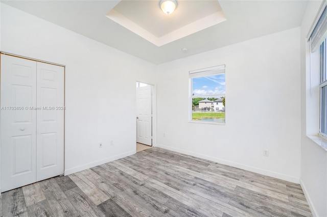 unfurnished bedroom with light hardwood / wood-style floors, a tray ceiling, and a closet