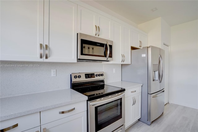 kitchen with light stone counters, light hardwood / wood-style flooring, white cabinets, and stainless steel appliances