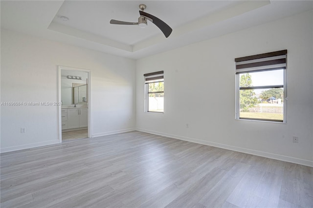 spare room featuring ceiling fan, light wood-type flooring, and a tray ceiling