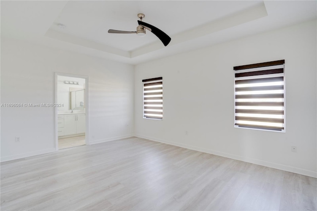 empty room with ceiling fan, a raised ceiling, and light hardwood / wood-style flooring