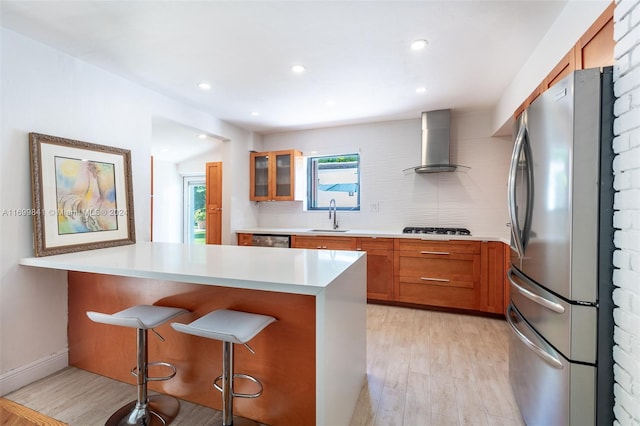 kitchen with sink, range hood, a breakfast bar, appliances with stainless steel finishes, and light wood-type flooring