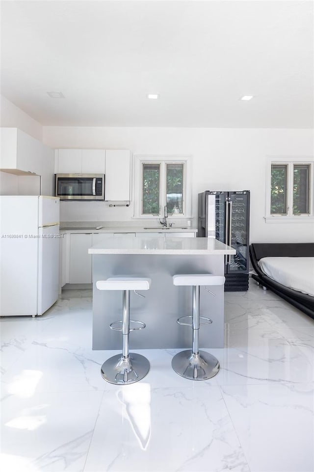 kitchen featuring a kitchen bar, a healthy amount of sunlight, white cabinets, and white fridge