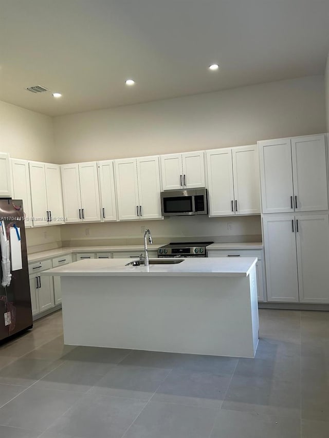 kitchen featuring white cabinets, light tile patterned floors, stainless steel appliances, and a kitchen island with sink