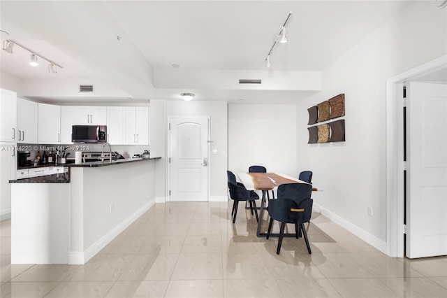 kitchen featuring white cabinets, kitchen peninsula, track lighting, and dark stone countertops