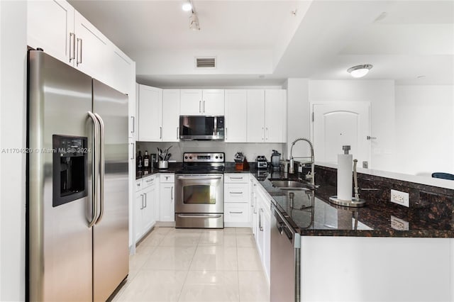 kitchen with white cabinetry, sink, stainless steel appliances, kitchen peninsula, and dark stone countertops