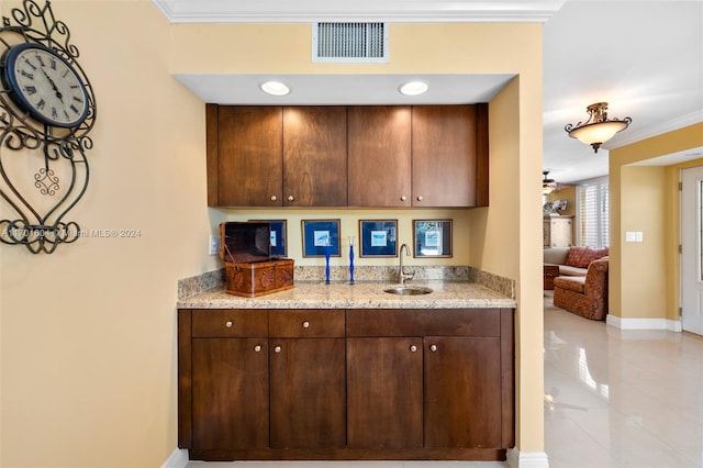 kitchen with light stone countertops, ornamental molding, dark brown cabinets, sink, and light tile patterned floors