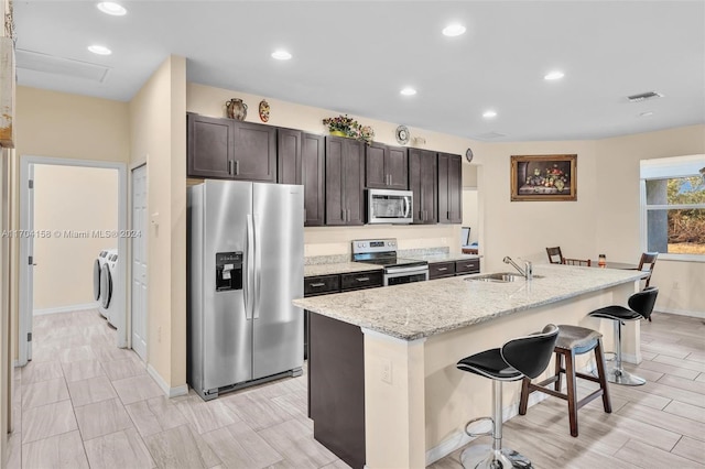 kitchen with a breakfast bar, a kitchen island with sink, sink, appliances with stainless steel finishes, and washing machine and clothes dryer