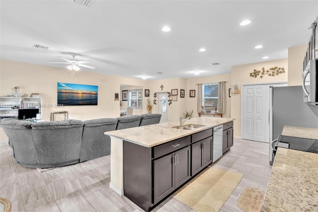 kitchen with dishwasher, a kitchen island with sink, sink, ceiling fan, and light stone countertops