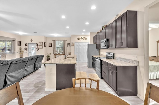 kitchen featuring light stone countertops, dark brown cabinetry, stainless steel appliances, sink, and an island with sink