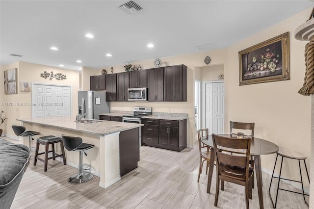 kitchen featuring a breakfast bar area, dark brown cabinetry, light stone counters, and appliances with stainless steel finishes