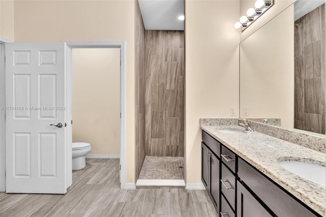 bathroom with tiled shower, hardwood / wood-style floors, vanity, and toilet