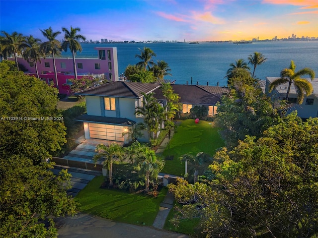 9301 N Bayshore Dr, Miami Shores, FL 33138 - view of front facade featuring a water view, a tiled roof, stucco siding, a garage, and a yard