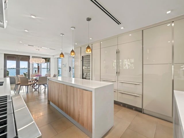 kitchen featuring light tile patterned floors, a water view, white cabinetry, hanging light fixtures, and a large island