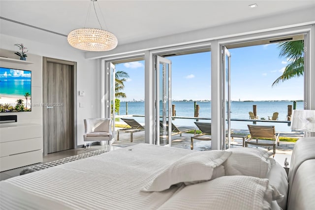 bedroom featuring access to outside, a water view, and an inviting chandelier