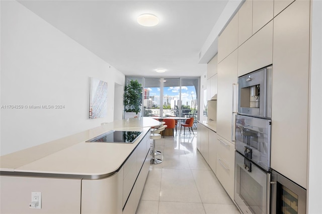 kitchen featuring black electric stovetop, stainless steel microwave, light tile patterned floors, and a wall of windows