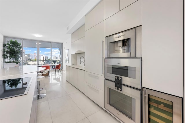 kitchen with floor to ceiling windows, light tile patterned floors, cooktop, wine cooler, and white cabinets