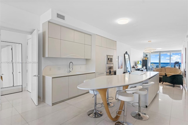 kitchen with expansive windows, sink, light tile patterned floors, a kitchen island, and a breakfast bar area