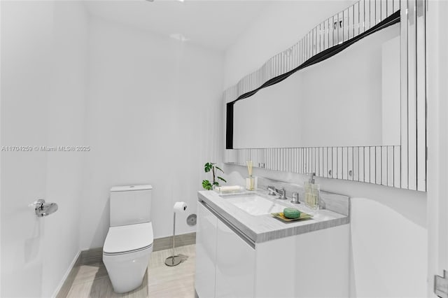 half bathroom featuring toilet, baseboards, and vanity