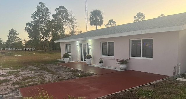 back of house at dusk with a patio and stucco siding