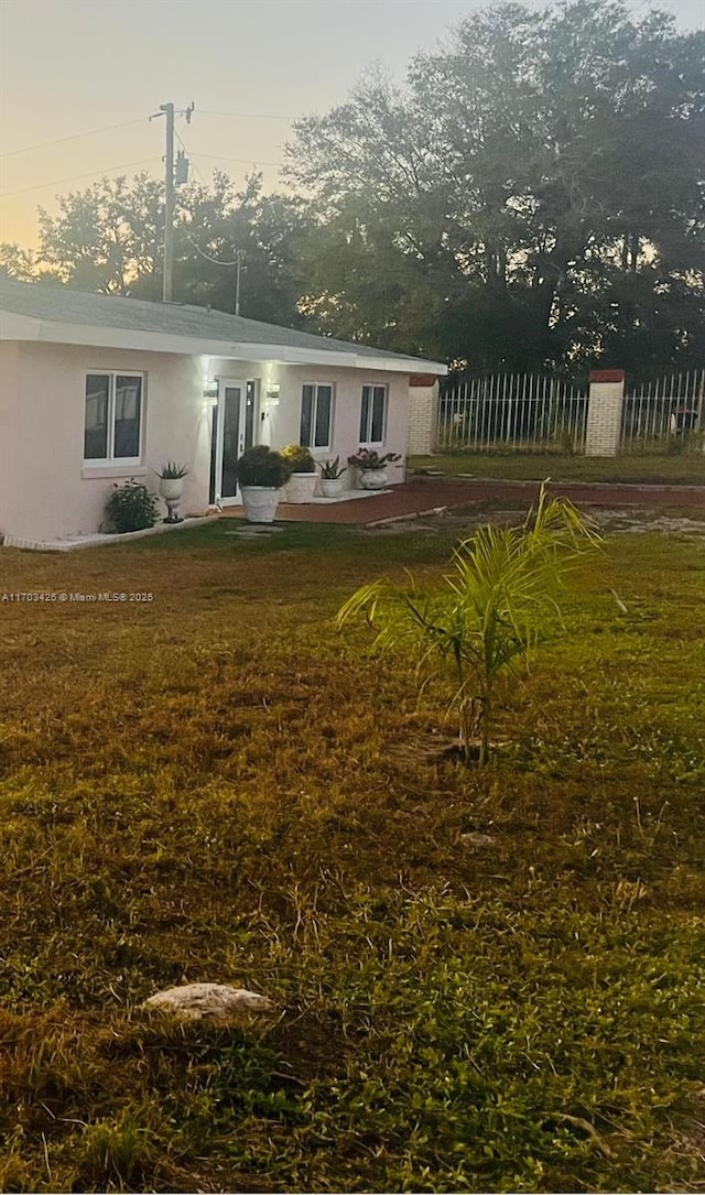 rear view of property with a lawn, fence, and stucco siding