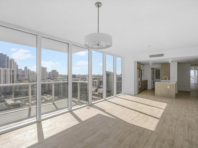 unfurnished living room featuring plenty of natural light, expansive windows, light wood-type flooring, and sink