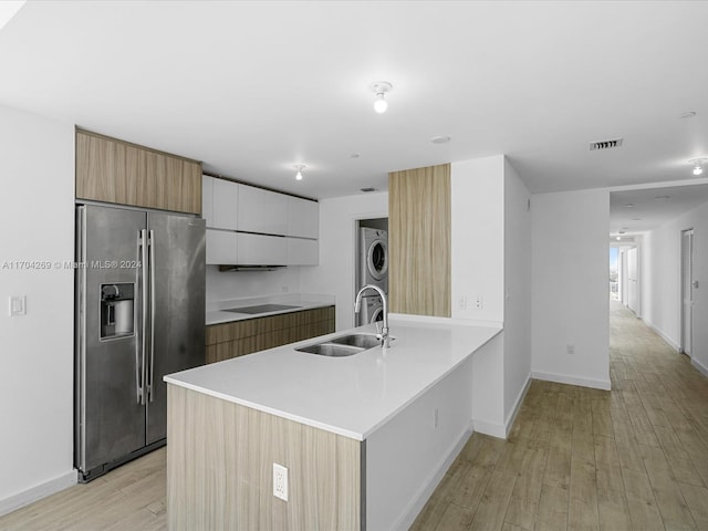 kitchen featuring white cabinetry, sink, stainless steel fridge with ice dispenser, stacked washer / drying machine, and light wood-type flooring